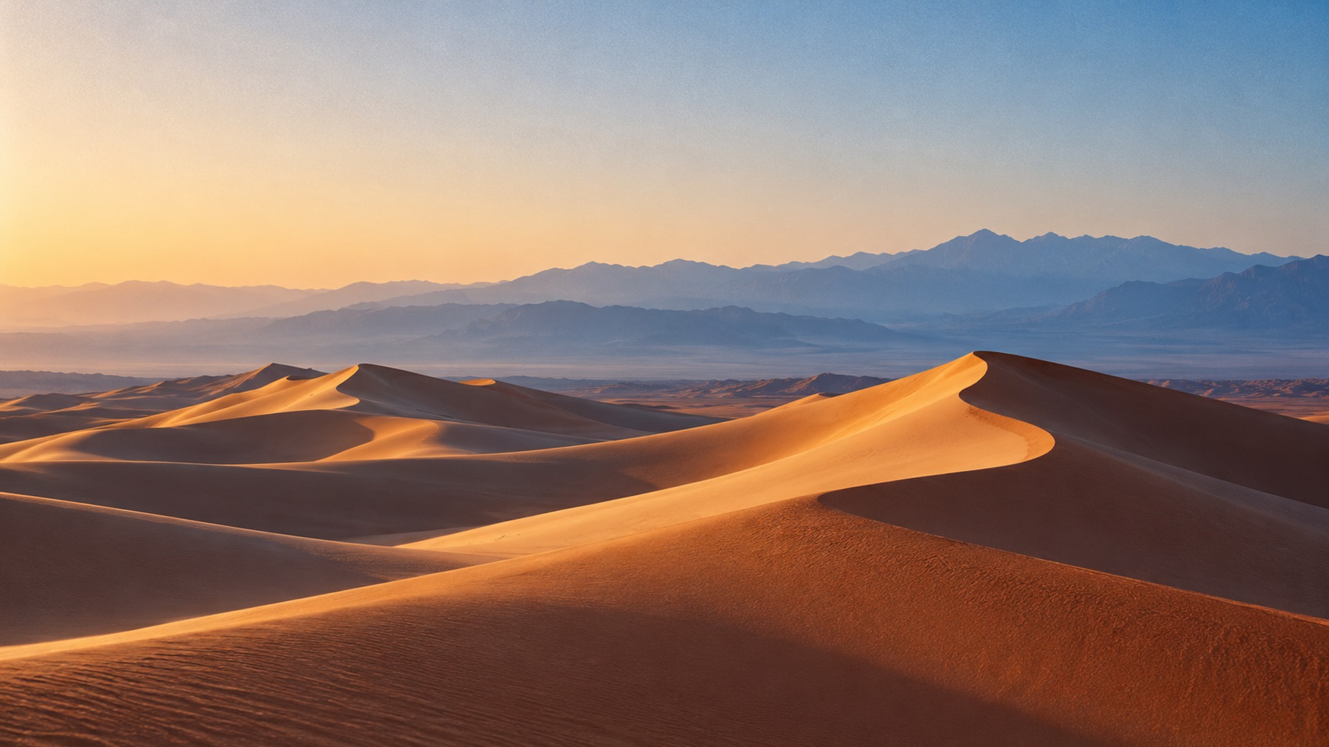 Sculptural rust-colored desert dunes fading into distant blue mountains.